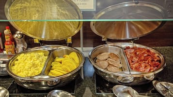 Un bufé con diferentes opciones de comida, incluyendo huevos revueltos, plátanos y carne.