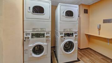A laundry room with two stacked washing machines and dryers, a wall-mounted phone, and a sign for assistance.