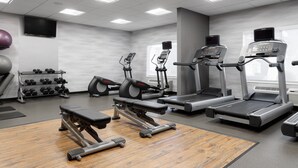 Ett gym med löpband, crosstrainers, en bänkpress och hantlar.