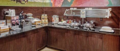 A breakfast bar with various food items and condiments, a coffee station, and a decorative mural with cows and flowers.