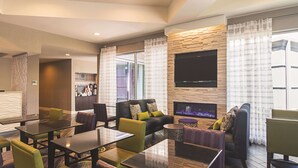 A modern hotel lobby with a seating area, a fireplace, and a television mounted on the wall. - La Quinta Inn & Suites by Wyndham Oklahoma City - NW Expwy (Oklahoma City)