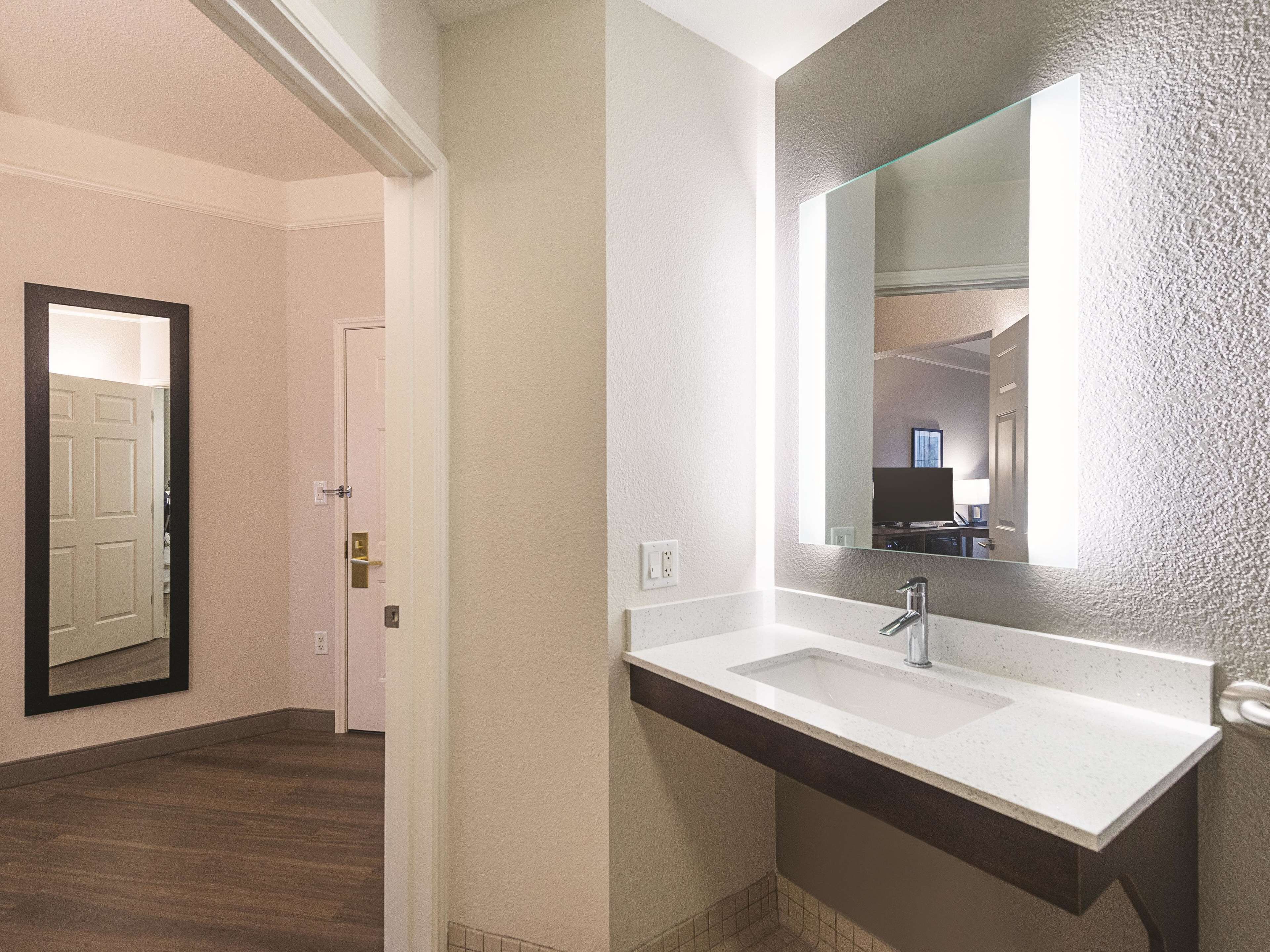 Un baño con un lavamanos blanco, un espejo grande y una puerta que da a otra habitación.