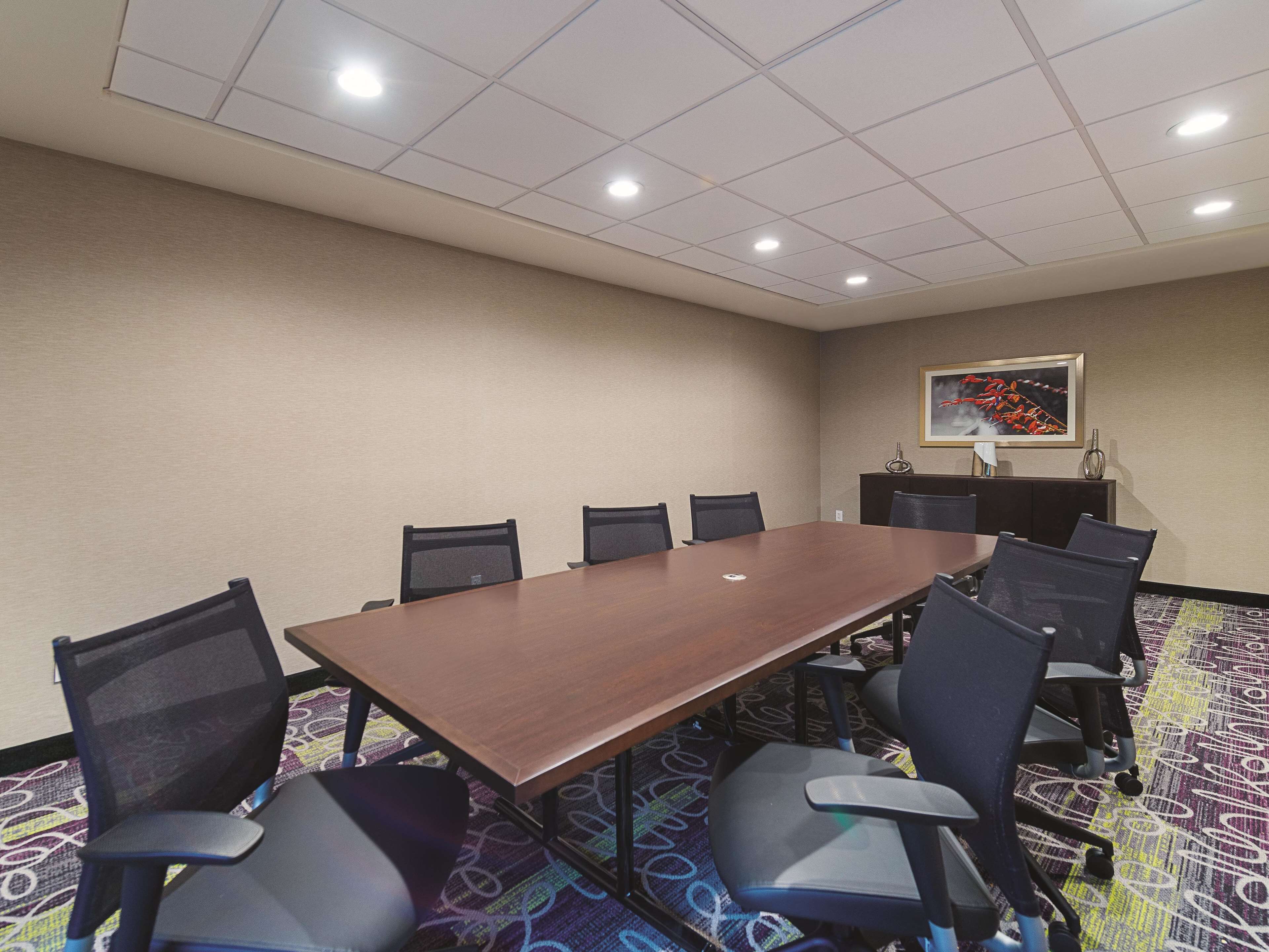 A conference room with a long table, chairs, a patterned carpet, and a ceiling with recessed lighting.