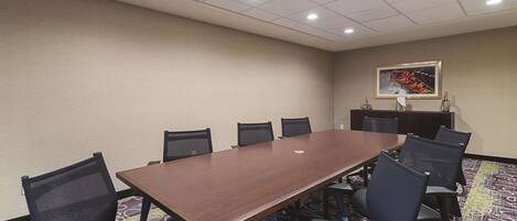 A conference room with a long table, chairs, a patterned carpet, and a ceiling with recessed lighting.