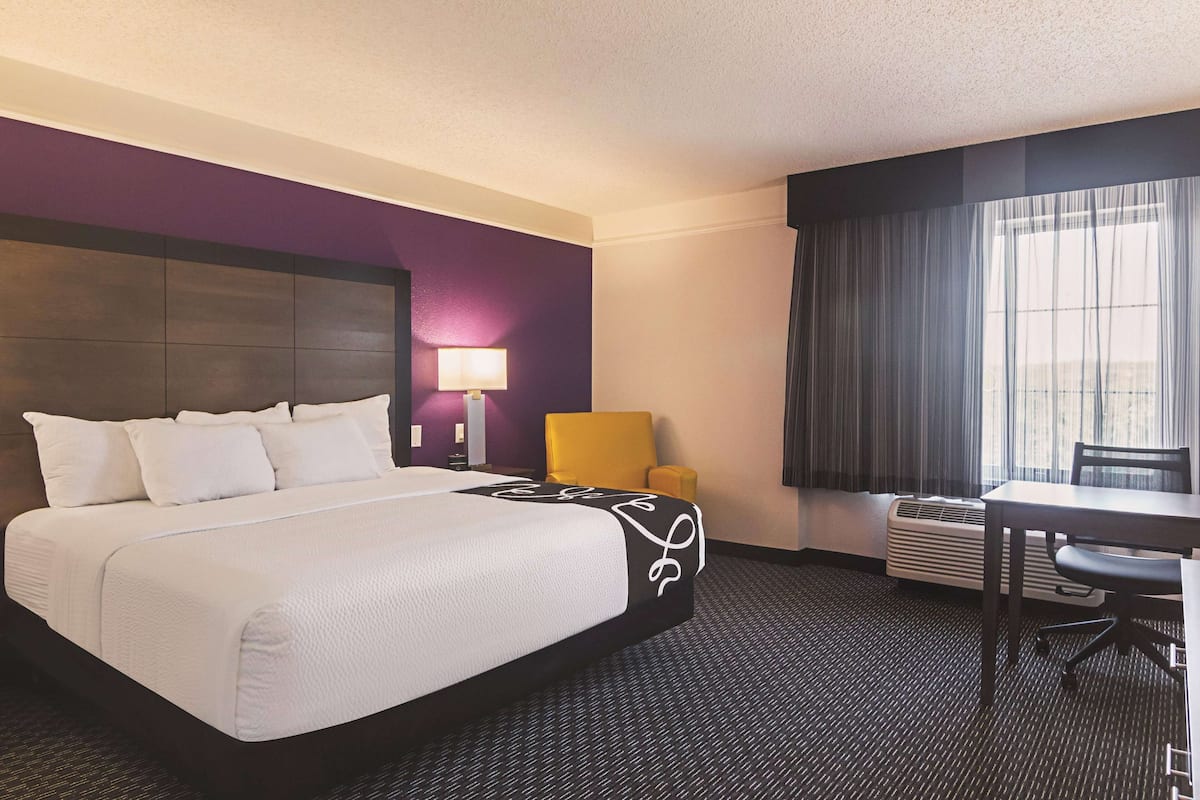 A hotel room with a large bed, a desk, a chair, a lamp, and a window with curtains.