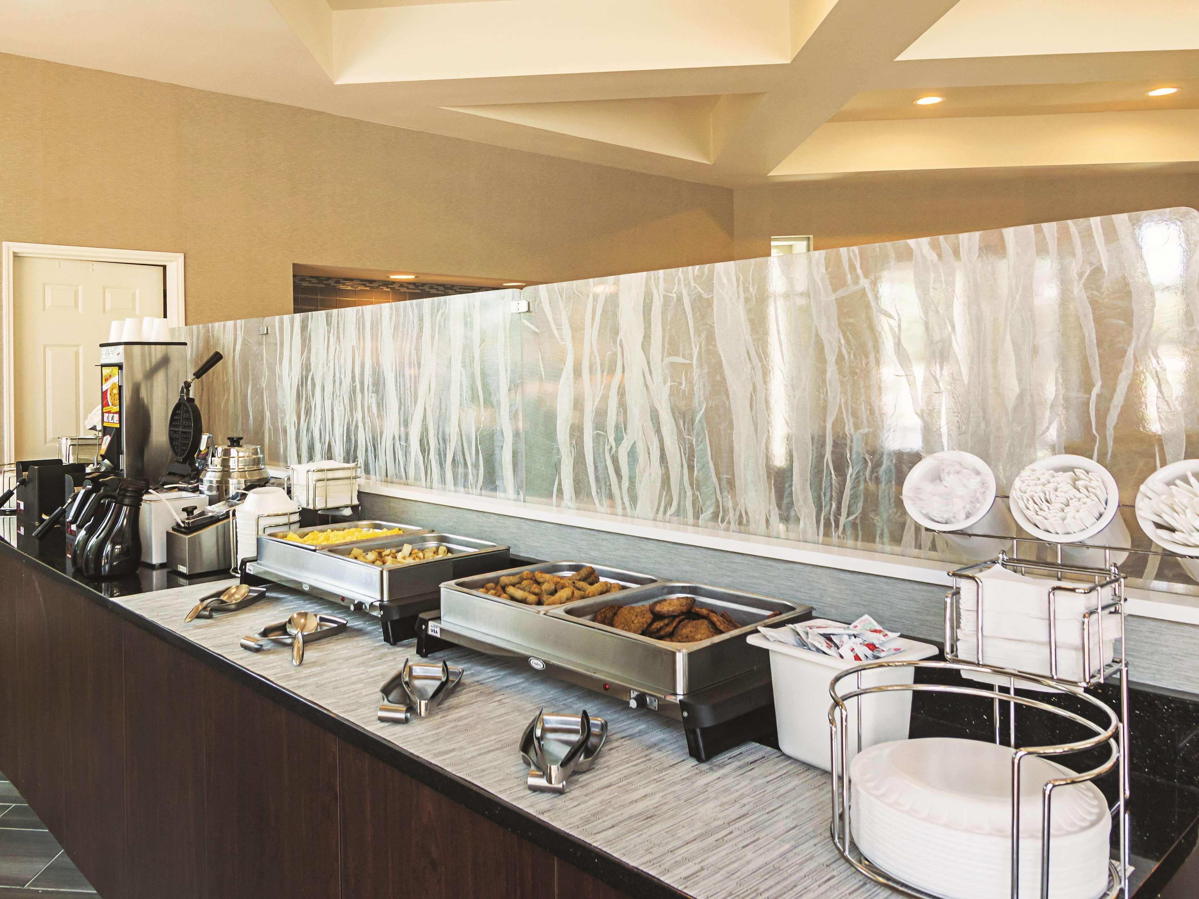 Un área de bufé con diferentes estaciones de comida, una máquina de café y una zona de estar con una silla blanca.