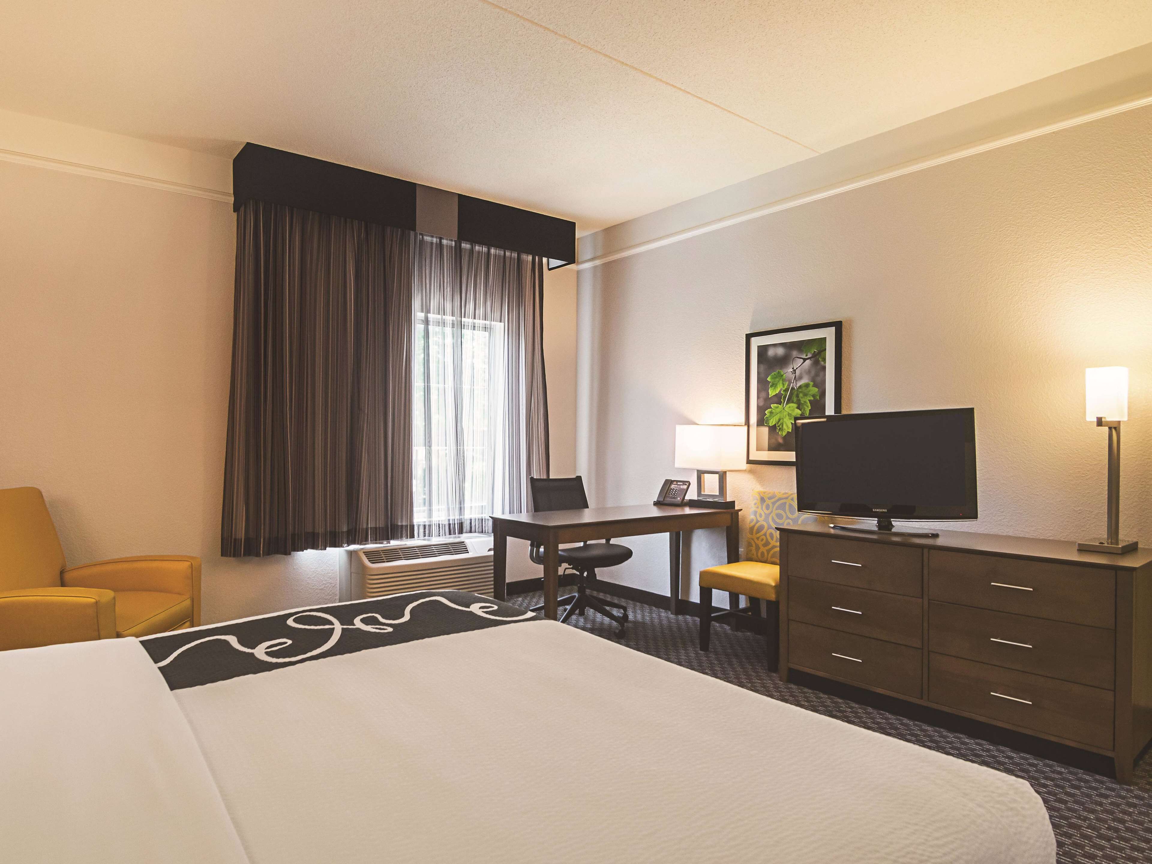 Une chambre d’hôtel équipée d’un lit, d’un bureau, d’une chaise, d’une télévision, d’une lampe et d’une fenêtre avec des rideaux.