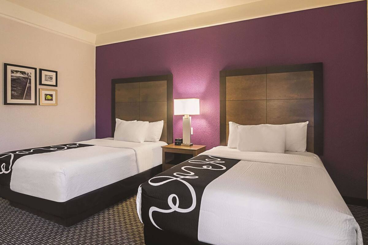 A hotel room with two beds, a nightstand with a lamp, and framed pictures on the wall.