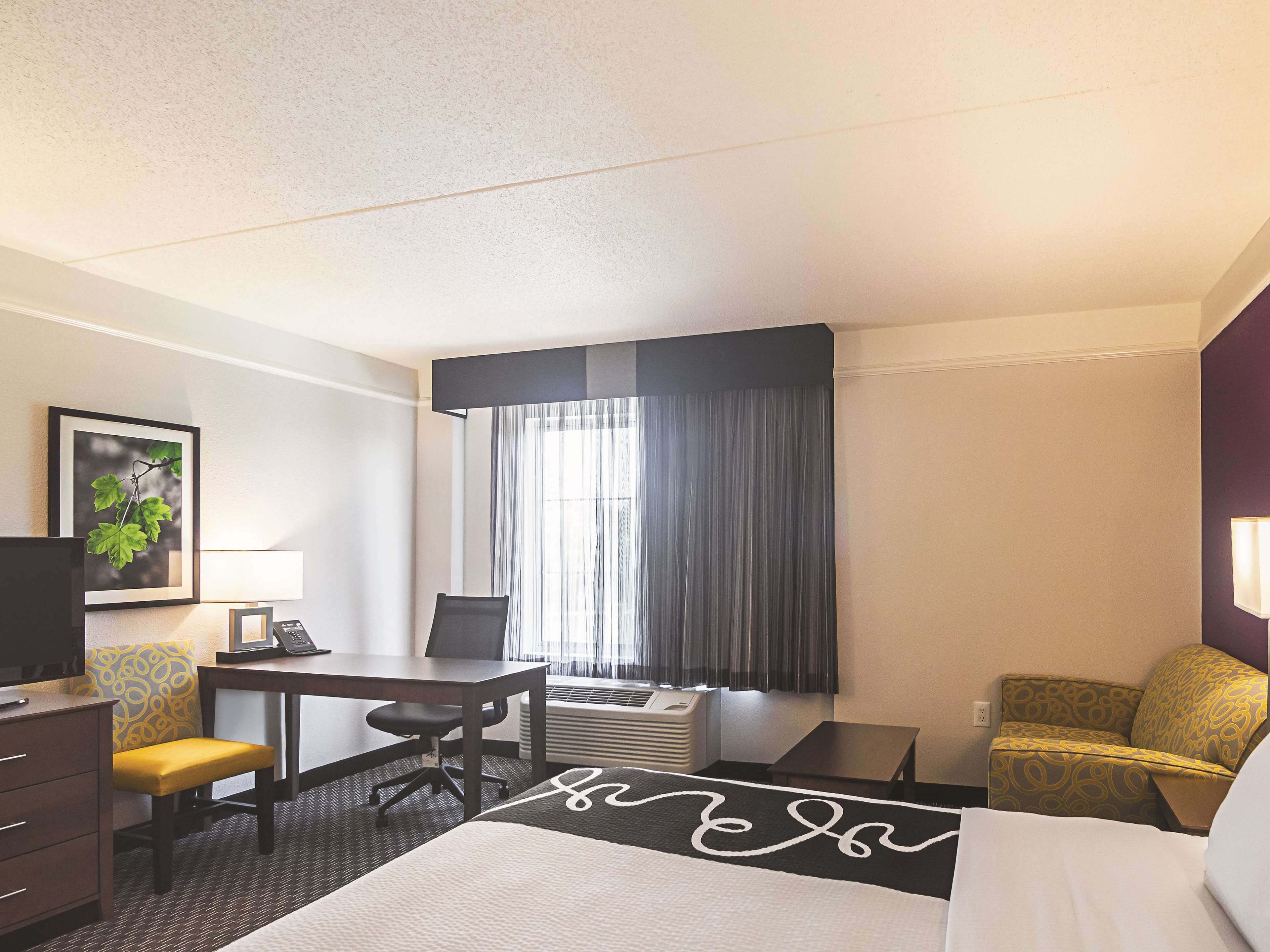 Ein Hotelzimmer mit Bett, Schreibtisch, Stuhl, Fernseher und einem Fenster mit Vorhängen.