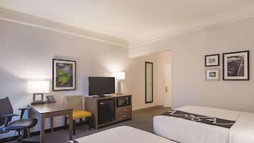 Quarto de hotel com uma cama, uma secretária com cadeira, televisão, luminária e quadros na parede.