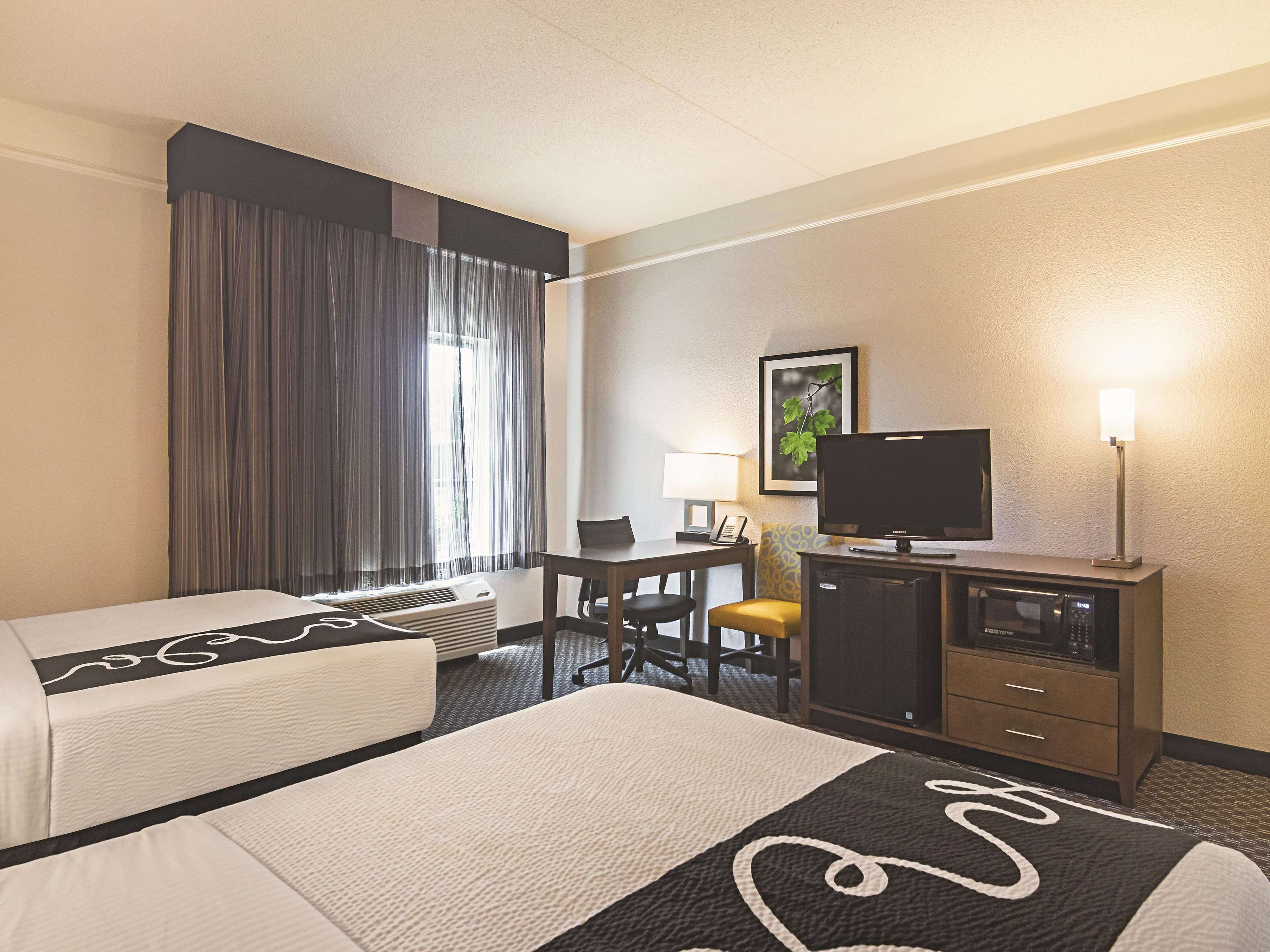 Habitación de hotel con dos camas, un escritorio, una silla, televisor, lámpara y microondas.