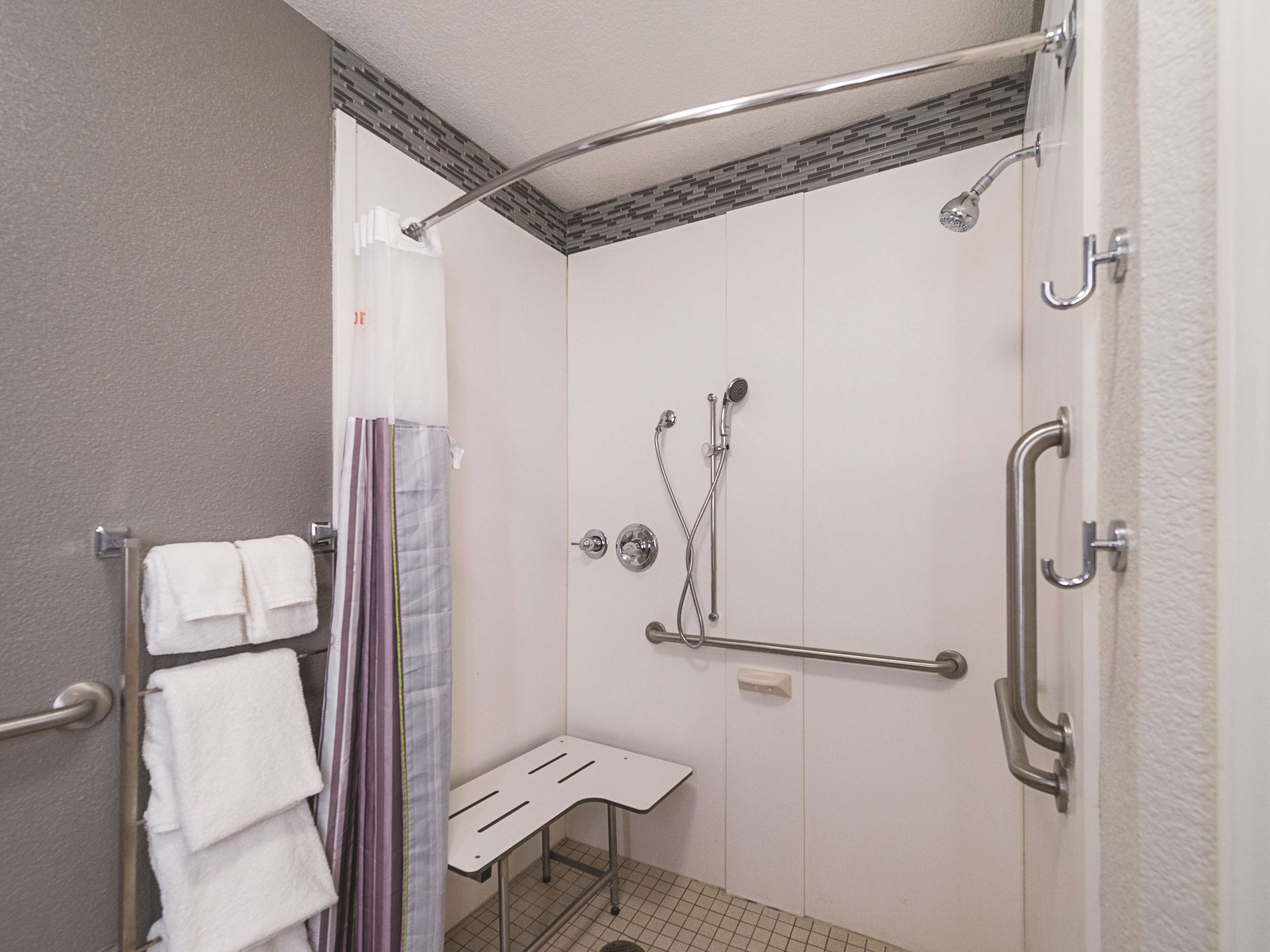 A shower area with a grab bar, a bench, and a towel rack.