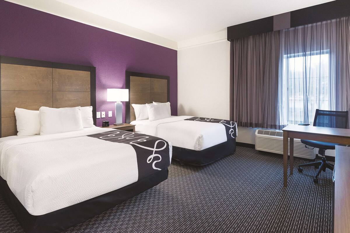 A hotel room with two beds, a desk, and a chair.