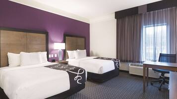 A hotel room with two beds, a desk, and a chair.