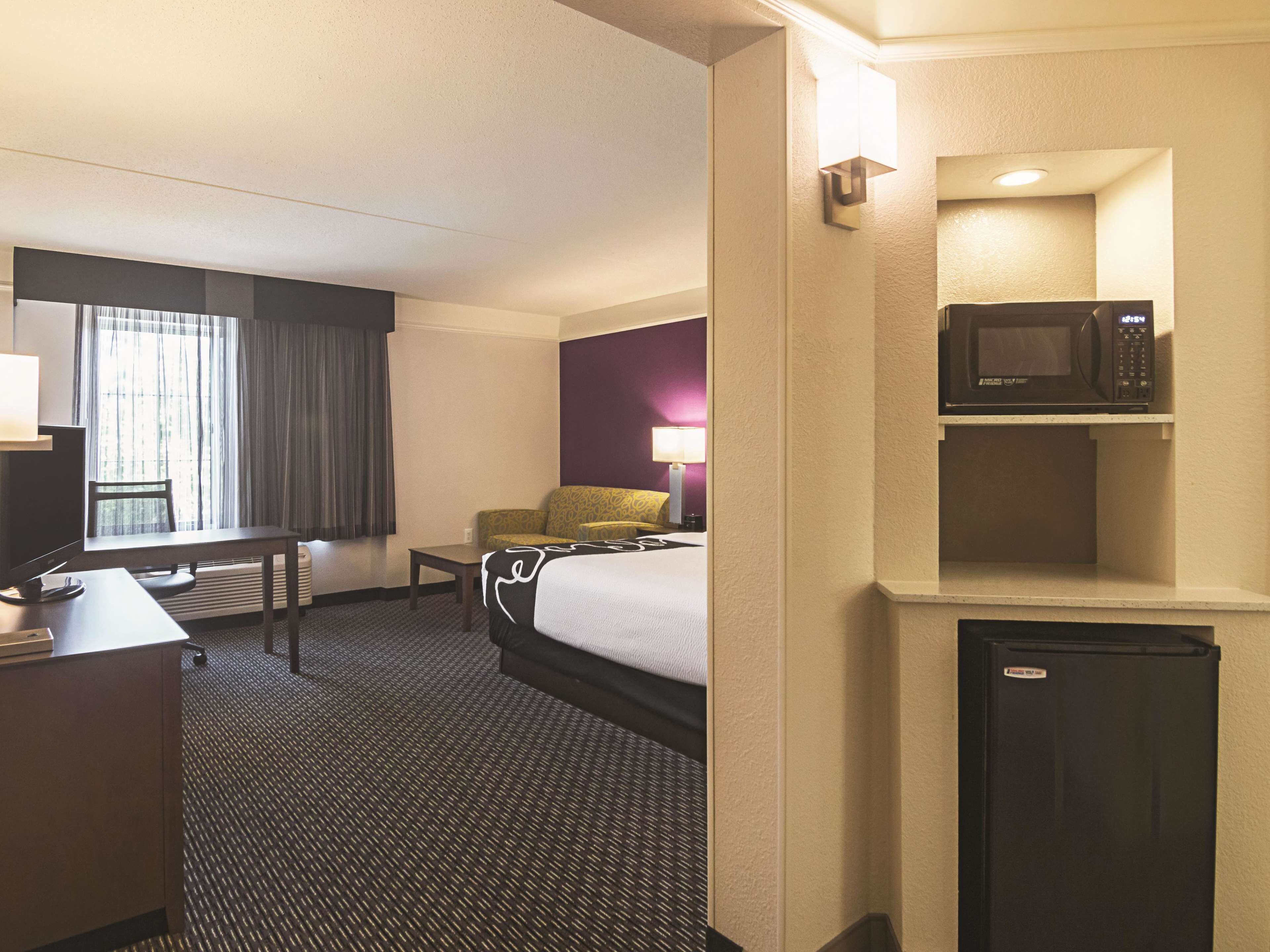 Habitación de hotel con cama, escritorio, silla, microondas y refrigerador pequeño.