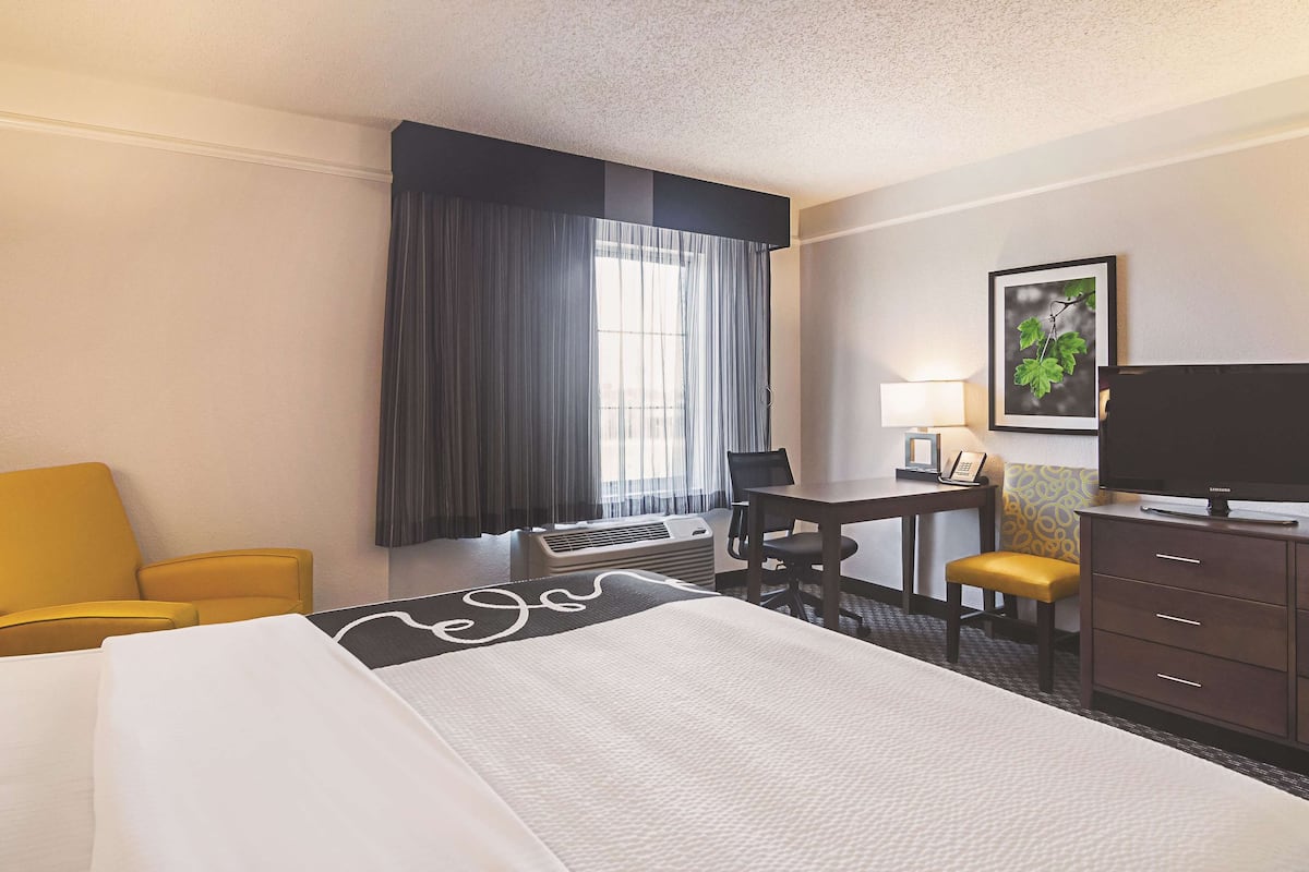 A hotel room with a bed, a desk, a chair, a television, and a window with curtains.