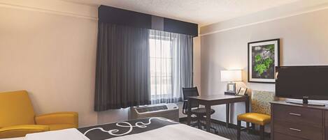 A hotel room with a bed, a desk, a chair, a television, and a window with curtains.