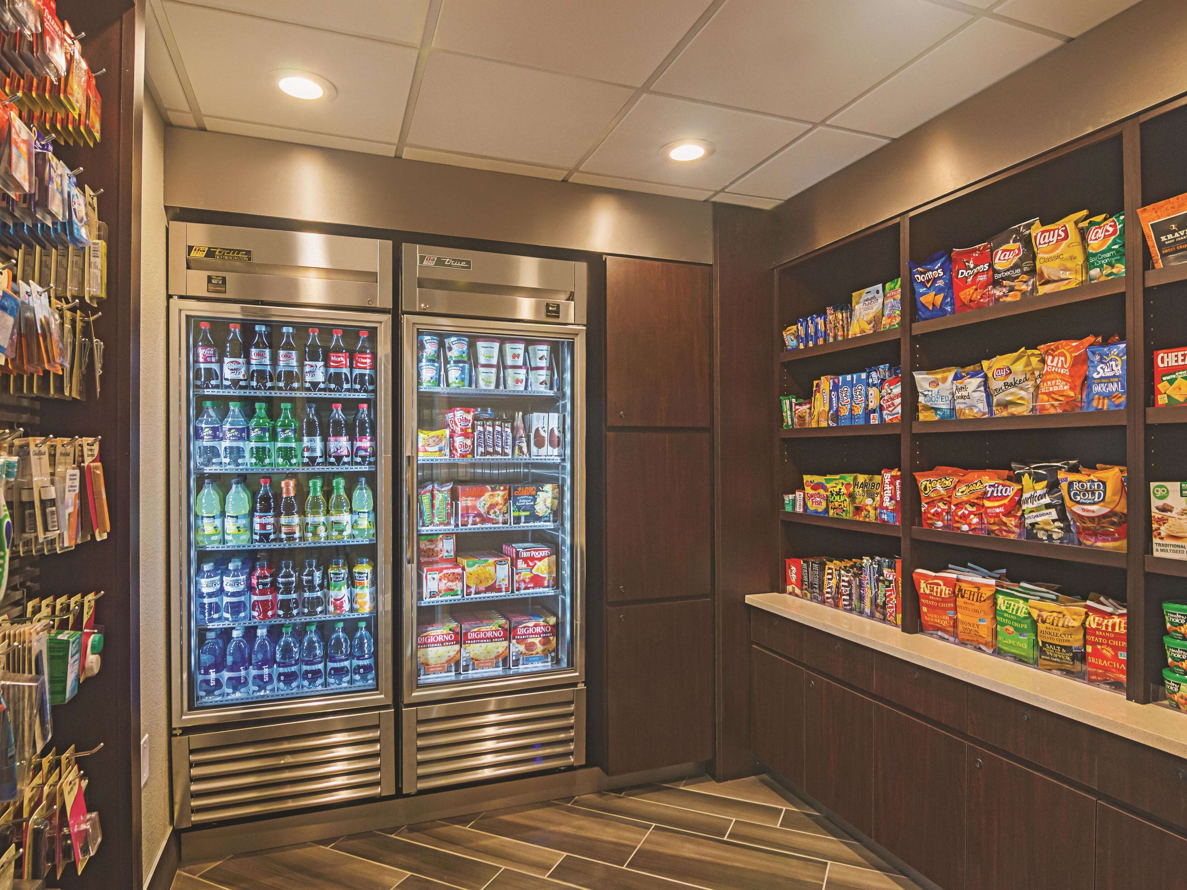 Un área de venta con dos dispensadores refrigerados para bebidas y estantes llenos de bocadillos y papas fritas.