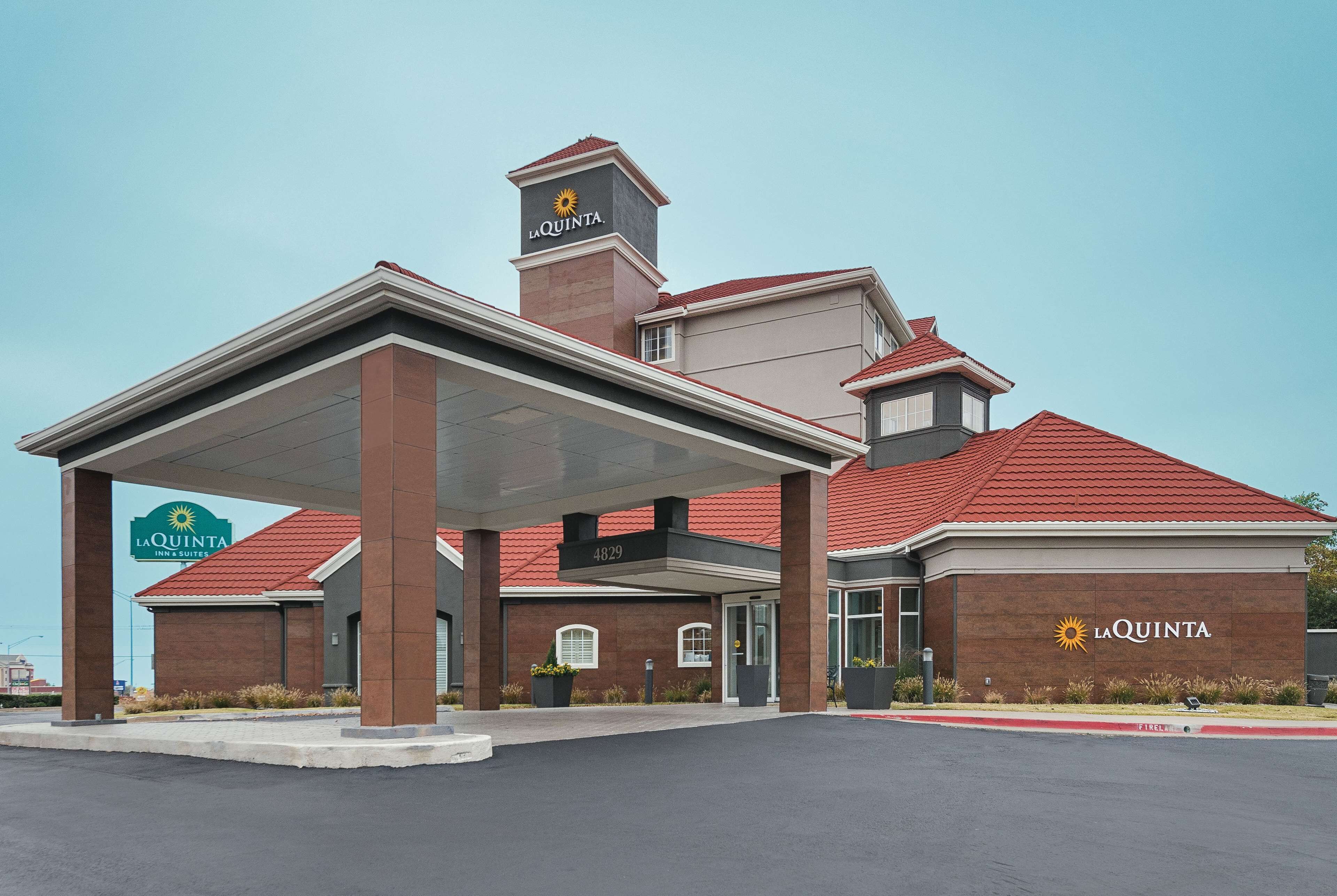 Un La Quinta Inn & Suites con un área exterior cubierta, fachada de ladrillo y techo de tejas rojas.