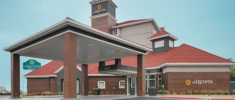 Un La Quinta Inn & Suites con un área exterior cubierta, fachada de ladrillo y techo de tejas rojas.