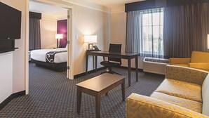 A hotel room with a bed, a desk with a chair, a sofa, a TV, and a window with curtains. - La Quinta Inn & Suites by Wyndham Oklahoma City - NW Expwy (Oklahoma City)