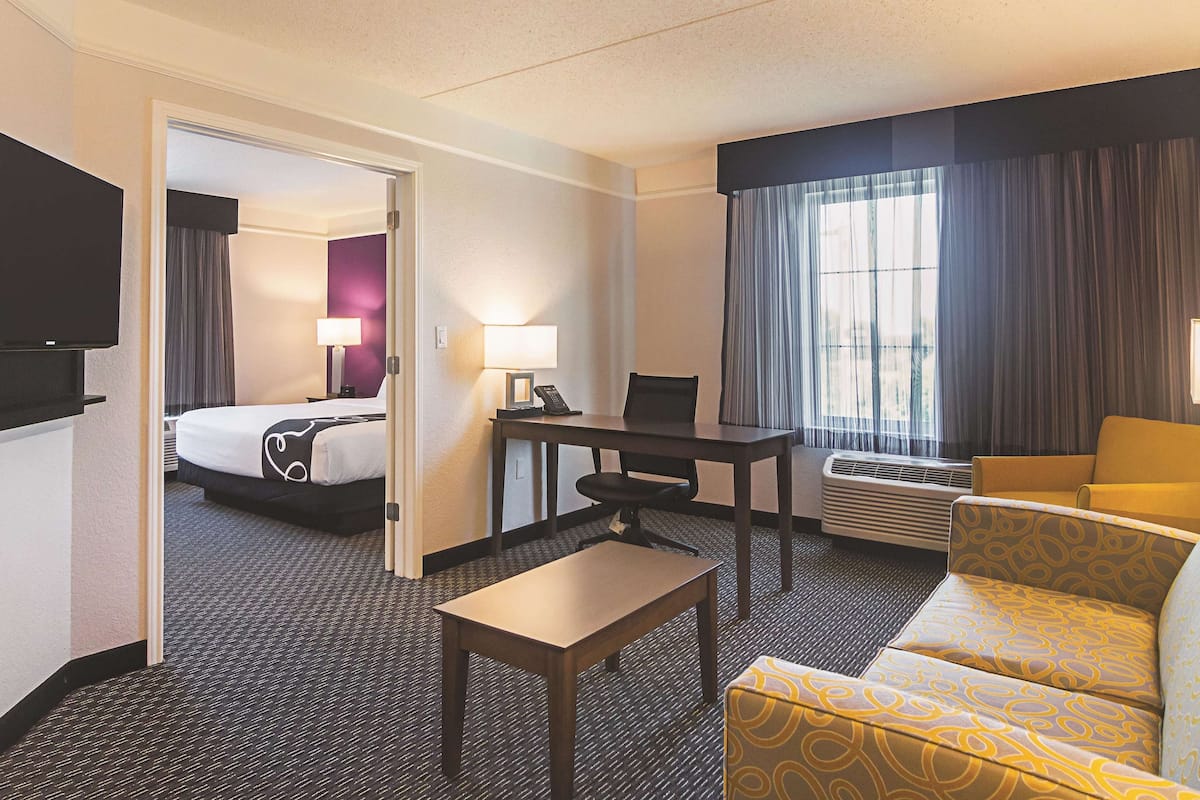 A hotel room with a bed, a desk with a chair, a sofa, a TV, and a window with curtains.