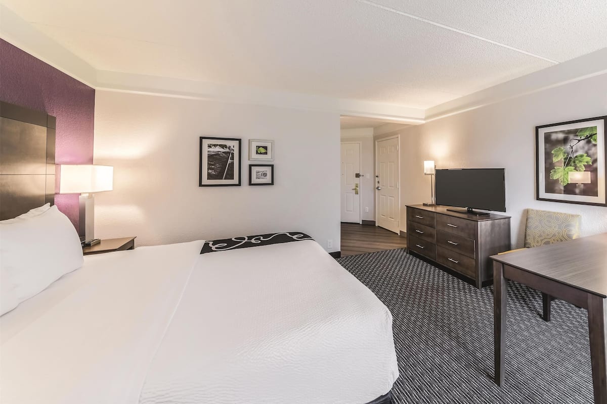Une chambre d’hôtel avec un grand lit, un bureau, une télévision et des tableaux encadrés accrochés au mur.