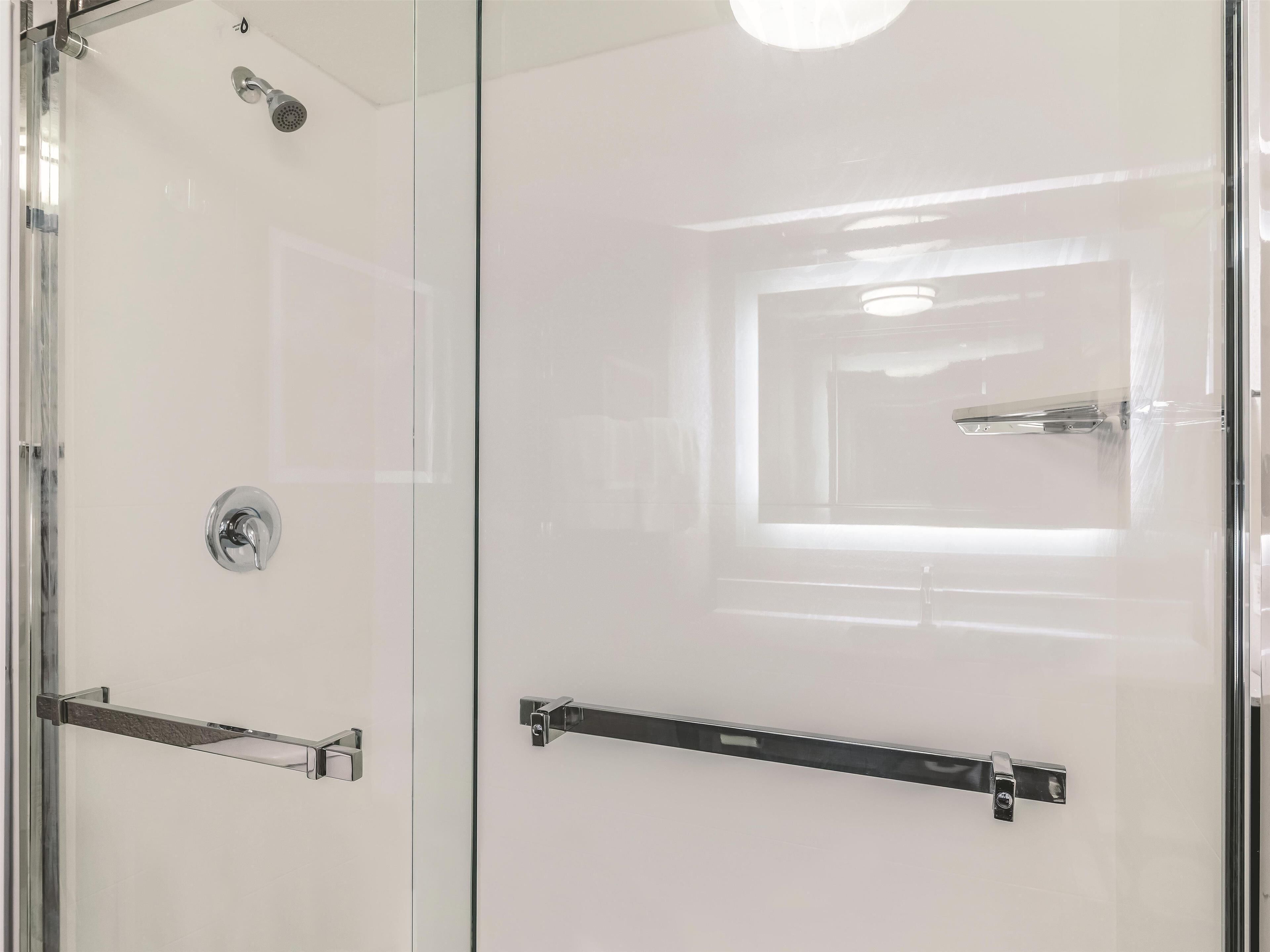 A modern bathroom with a glass shower enclosure, a handheld showerhead, and a towel rack.
