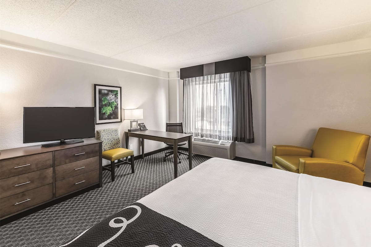 Une chambre d’hôtel équipée d’un lit, d’un bureau, d’une chaise, d’une télévision et d’une fenêtre avec des rideaux.