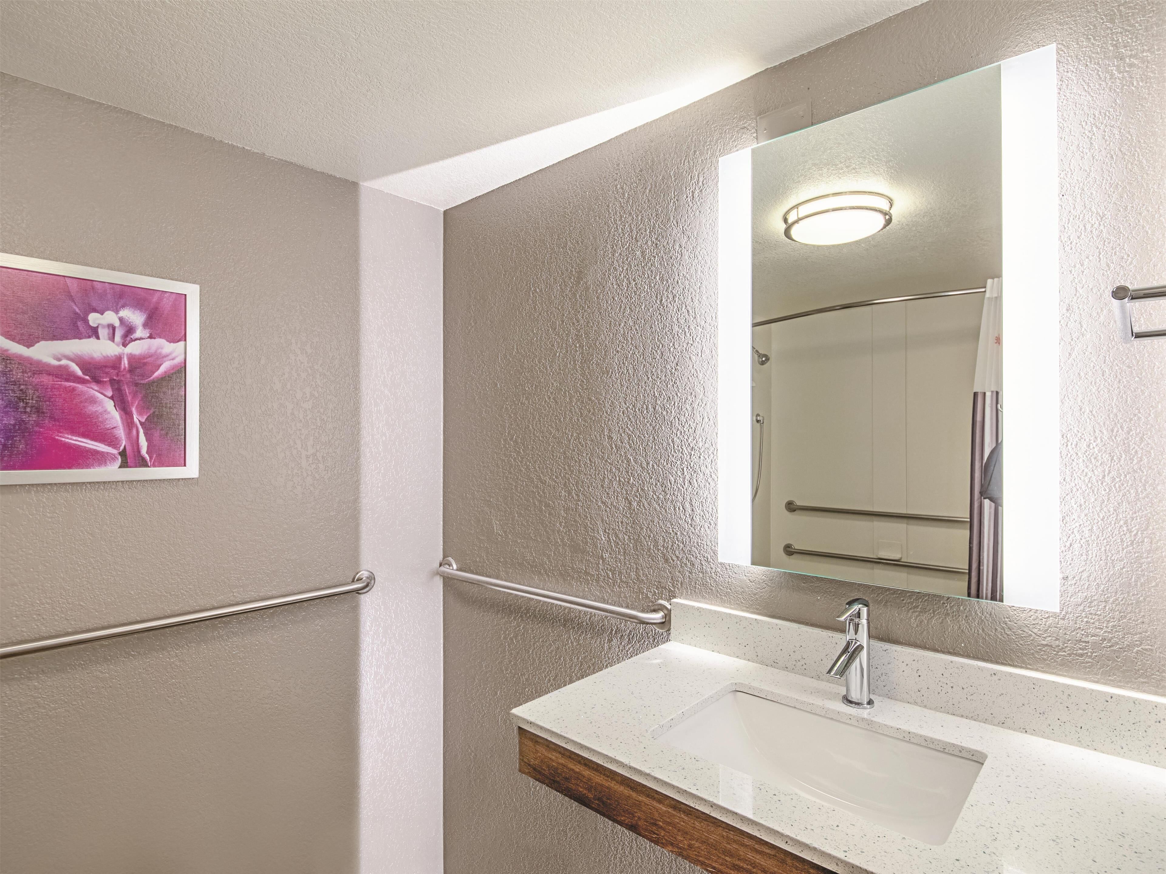 A bathroom with a white sink, a mirror, and a handrail.