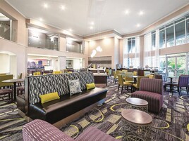 Un amplio vestíbulo de hotel con diseño moderno, que cuenta con una zona de estar central con un sofá estampado y varias mesas y sillas para comer.