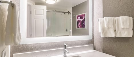 A bathroom with a large mirror, a sink, and a shower.