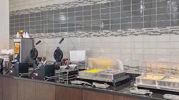 Un bar pour le petit-déjeuner équipé d’un appareil à gaufres, d’une machine à café et de différents récipients pour aliments.