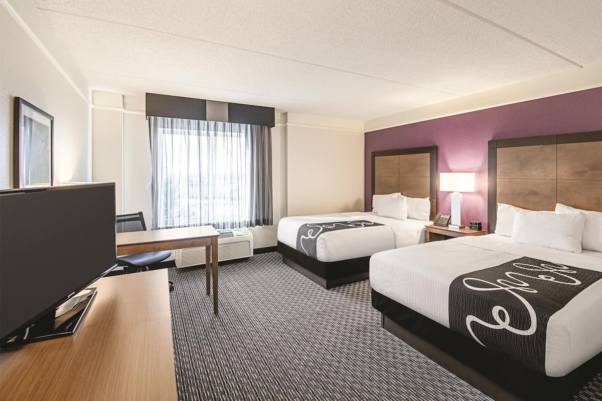 Une chambre d’hôtel avec deux lits, un bureau, une télévision et une fenêtre avec des rideaux.