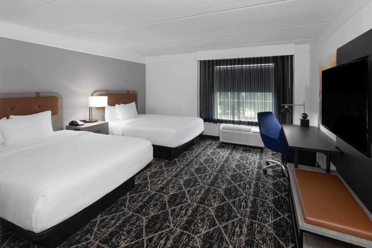 Een hotelkamer met twee bedden, een bureau, een stoel, een televisie en een raam met gordijnen.