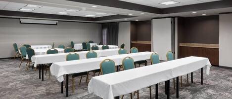 A conference room with multiple tables and chairs, a projector screen, and a large screen on the wall.