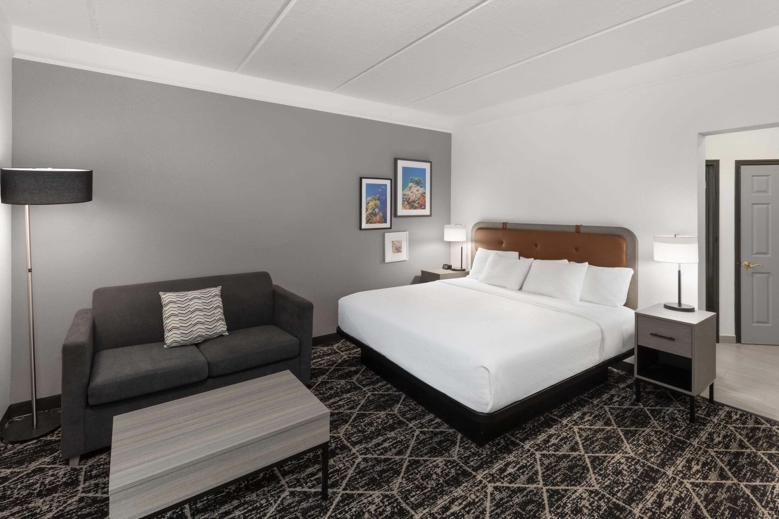 A hotel room with a bed, a sofa, a coffee table, a lamp, and a nightstand.