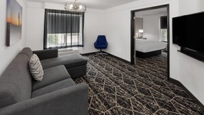 Een hotelkamer met een grijze bank, een blauwe stoel, een groot bed, een televisie en een kamerbreed tapijt met een patroon.