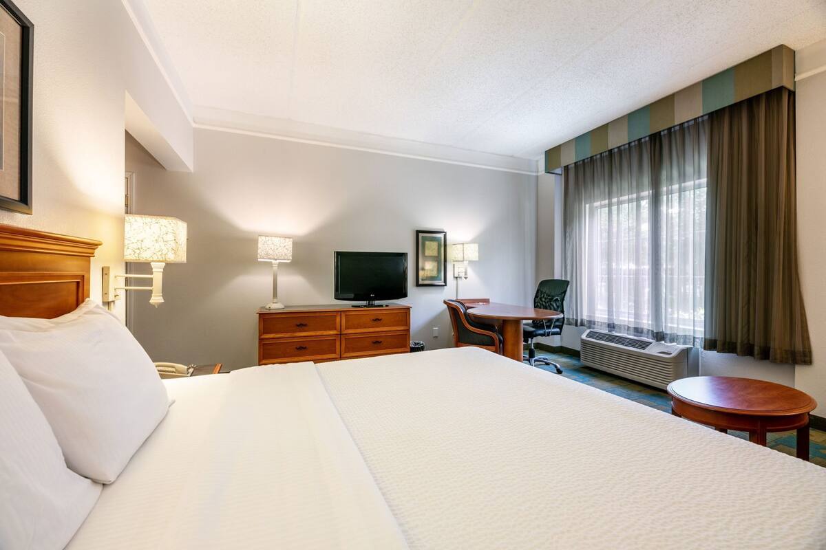 Een hotelkamer met een groot bed, een bureau, een televisie en een raam met gordijnen.