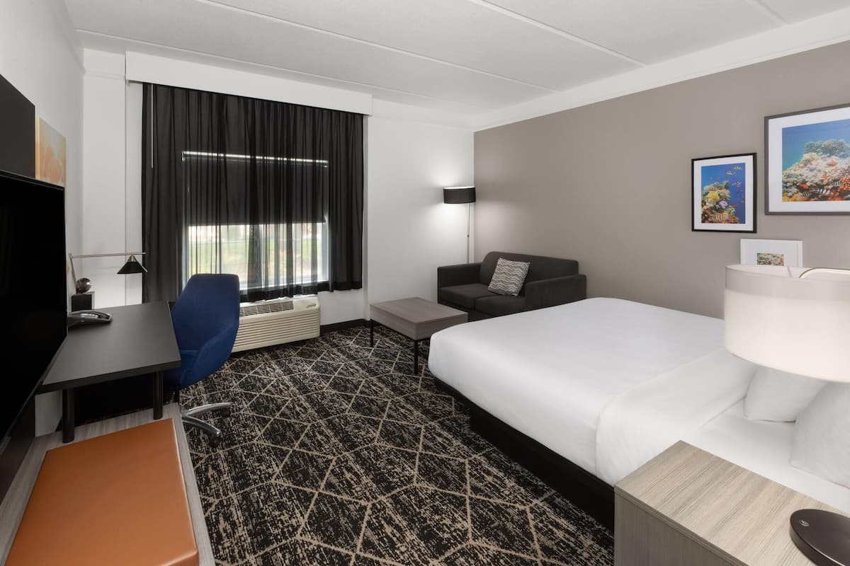 Een hotelkamer met een bed, een bureau, een stoel, een bank, een lamp en een raam met gordijnen.