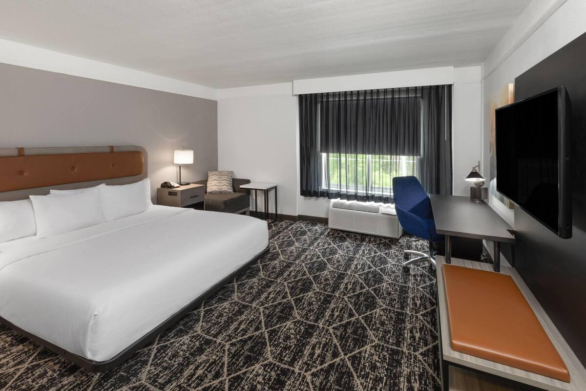 Een hotelkamer met een groot bed, een bureau, een stoel, een televisie en een raam met gordijnen.