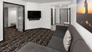 Een moderne hotel lobby met een grijze bank, een flatscreen televisie, een kamer met een patroon en een groot schilderij van een zonsondergang.
