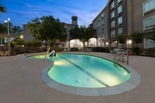 Une piscine à bordures courbes, entourée d’une clôture, et située à côté d’un bâtiment doté de nombreuses fenêtres et de balcons.