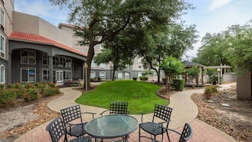 A courtyard with a paved walkway, a grassy area, and outdoor seating with chairs and a table.