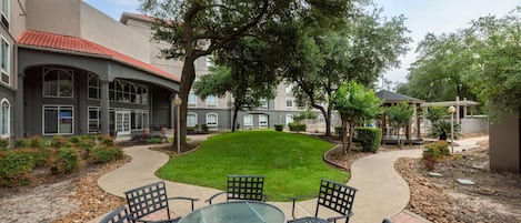 A courtyard with a paved walkway, a grassy area, and outdoor seating with chairs and a table.