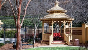 A gazebo with a red bench and a small table, surrounded by a fence and trees. - La Quinta by Wyndham Haywood Mall-Near Greenville Downtown (Greenville)