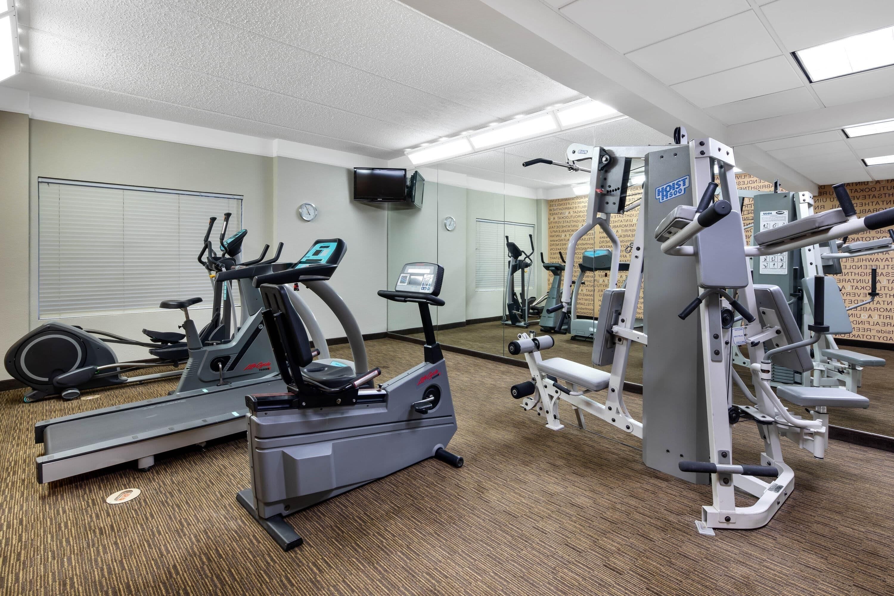 A gym with cardio machines, weight machines, and a TV screen.