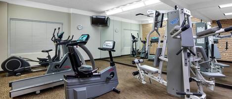 A gym with cardio machines, weight machines, and a TV screen.