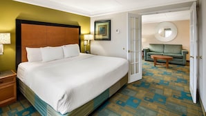 A hotel room with a large bed, a sofa, a round mirror, and a patterned carpet. - La Quinta by Wyndham Haywood Mall-Near Greenville Downtown (Greenville)