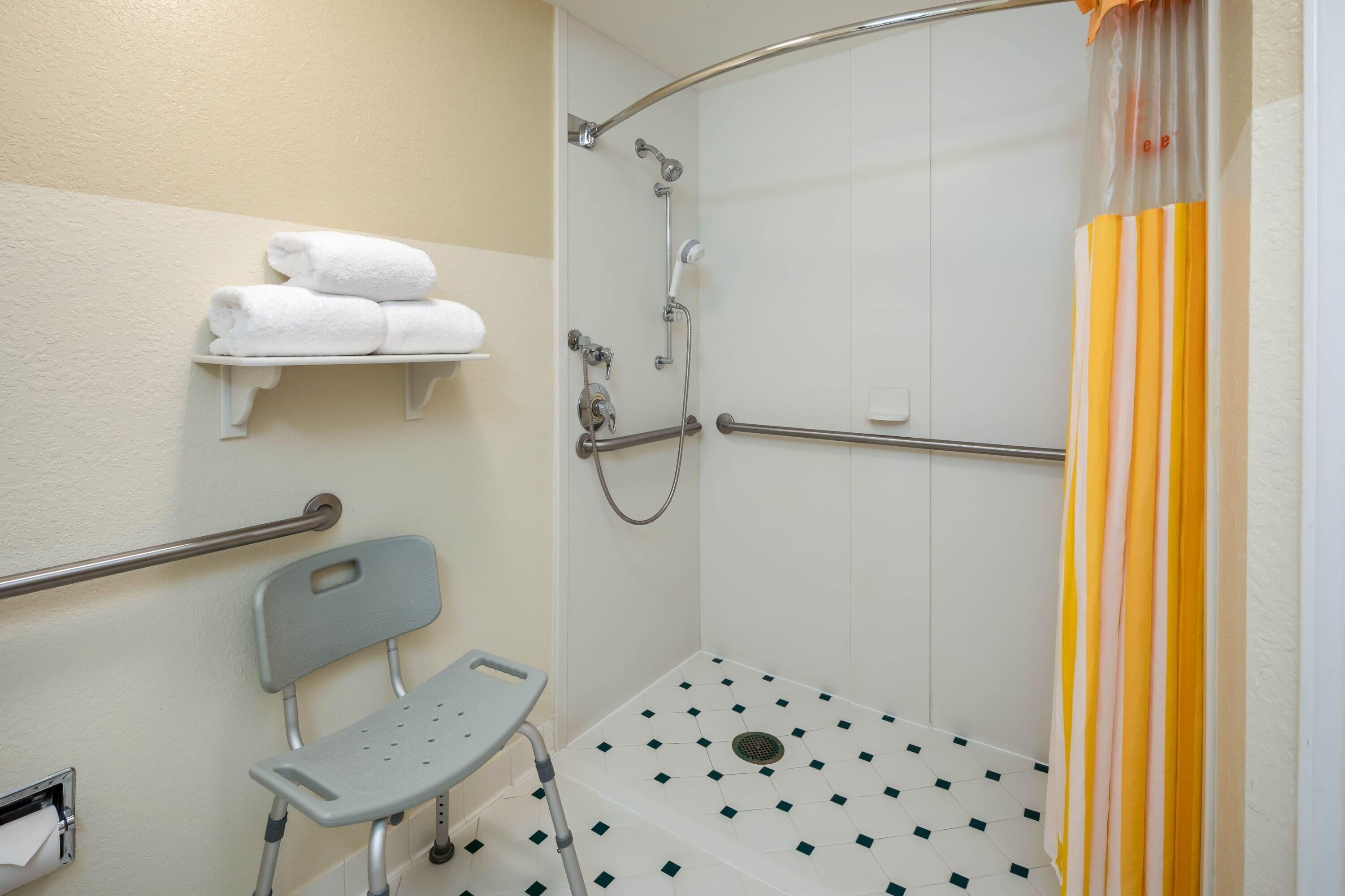 Une douche accessible aux personnes en fauteuil roulant, équipée de barres d’appui, d’un banc et d’un porte-serviettes.